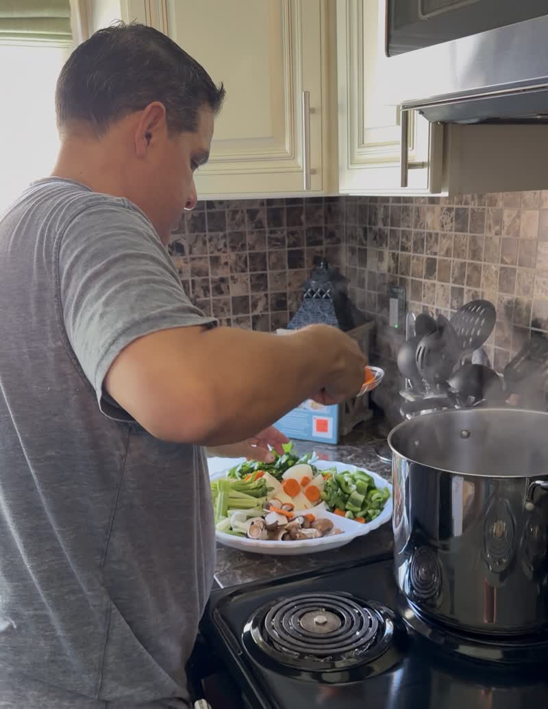 John adding cut vegetables to a steaming pot on the stove
